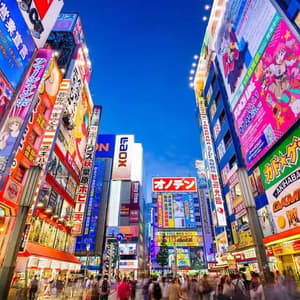 Una trafficata strada cittadina al tramonto è affiancata da alti edifici coperti da luminosi e colorati cartelloni e pubblicità giapponesi.