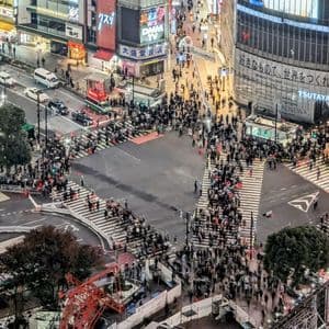 Una vista aerea di un vivace incrocio cittadino di notte, dove folle di persone con effetto mosso attraversano le strade tra alti edifici illuminati.