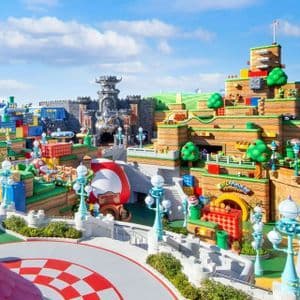 Una vista grandangolare e colorata di un parco divertimenti a tema Super Mario, con il Castello di Bowser e colline in stile videogioco sotto un cielo blu.