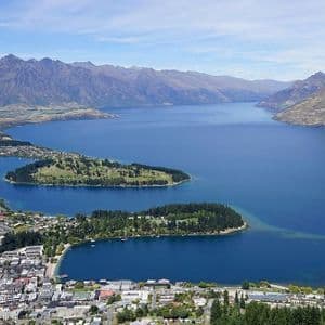 Vista aerea di una cittadina lacustre e isolotti su un grande lago blu, con una catena montuosa scoscesa sullo sfondo.