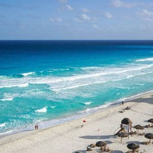 Vista aerea di una spiaggia di sabbia bianca con acqua turchese dove le persone si rilassano sotto ombrelloni di paglia.