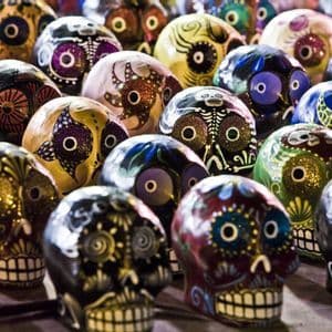Una collezione di teschi calavera colorati e dipinti a mano, decorati con motivi intricati e glitter, esposti insieme.