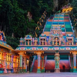 La scalinata colorata e illuminata di un sontuoso complesso templare, incastonata nel fianco di una ripida scogliera verde.