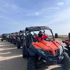 Un viaggio di gruppo WeRoad con una lunga fila di buggy fuoristrada arancioni su un sentiero sabbioso sotto un cielo azzurro limpido.