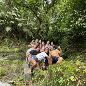 Eine WeRoad-Gruppe lächelt und posiert für ein Foto auf moosbewachsenen Felsen in einem dichten grünen Dschungel.