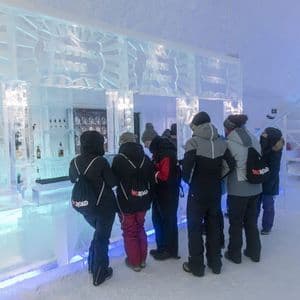 Un groupe WeRoad portant des vestes d'hiver se tient au comptoir d'un bar entièrement fait de glace.