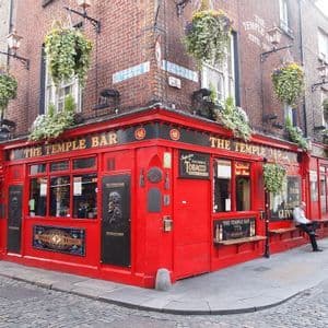 Eckansicht der roten Fassade des Pubs The Temple Bar in einer Kopfsteinpflastergasse, geschmückt mit Hängepflanzen.