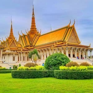 An ornate palace with a golden roof and spires stands behind a manicured green lawn with trimmed hedges.