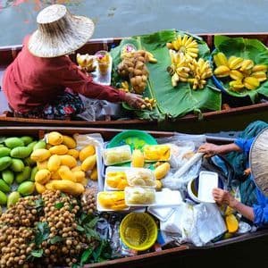 An overhead view of two vendors in conical hats selling fresh fruit like bananas and mangoes from their long wooden boats at a floating market.