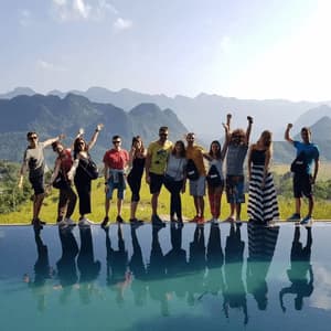 Un gruppo WeRoad in viaggio posa al bordo di una piscina a sfioro, con i riflessi nell'acqua e un paesaggio montuoso sullo sfondo.