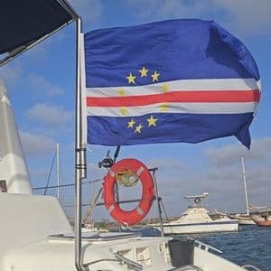 The flag of Cape Verde waving in the wind, mounted on the back of a boat in a marina under a blue sky.