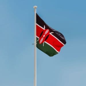 La bandera nacional de Kenia ondeando en un mástil blanco contra un cielo azul claro.