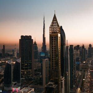 Una vista panoramica di un moderno skyline cittadino con grattacieli al tramonto, e sotto autostrade trafficate e una linea della metropolitana.