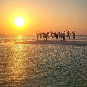 Eine WeRoad-Gruppe springt als Silhouette auf einer Sandbank, während die Sonne über dem ruhigen Meer versinkt.