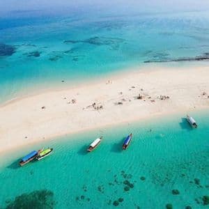 Luftaufnahme einer WeRoad Gruppenreise auf einer weißen Sandbank, mit mehreren Booten, die im klaren türkisfarbenen Wasser schwimmen.
