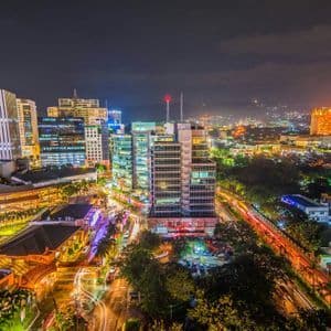 Una vista dall'alto di un paesaggio urbano moderno di notte, con grattacieli illuminati e scie luminose a lunga esposizione delle auto sulle strade trafficate.