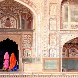 Due donne in sari colorati attraversano un portale ad arco di un palazzo riccamente decorato con affreschi dettagliati.