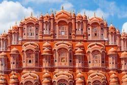 La facciata rosa e riccamente decorata di un edificio storico a più piani, con numerose piccole finestre ad arco, sotto un cielo blu e nuvoloso.