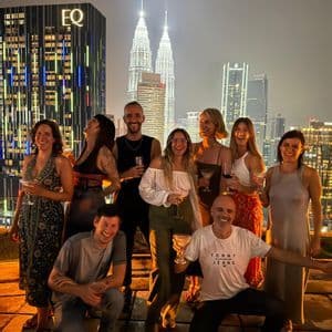 Un grupo de WeRoad sonríe y posa con bebidas en una azotea de noche, con el horizonte de una ciudad iluminada de fondo.