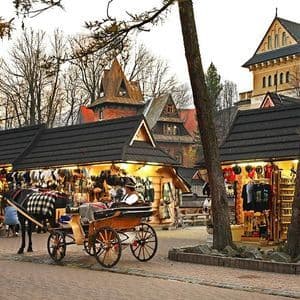 Une calèche est garée sur une rue pavée, à côté d'étals de marché en bois éclairés, avec des bâtiments rustiques et des arbres en arrière-plan.