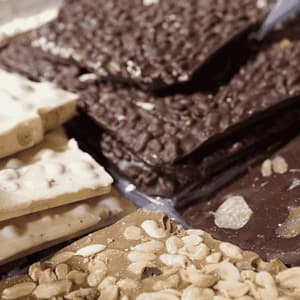 Primer plano de cortezas de chocolate artesanales variadas, que incluyen chocolate blanco, con leche y negro, con aderezos como frutos secos y frutas confitadas.