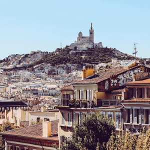 Una grande chiesa si erge su una collina verde che domina una città con edifici dai tetti in terracotta sotto un cielo azzurro e limpido.