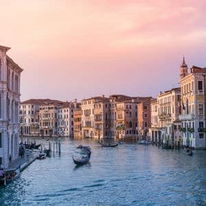 Góndolas y barcos navegan por un ancho canal rodeado de edificios históricos bajo un cielo de atardecer rosado.