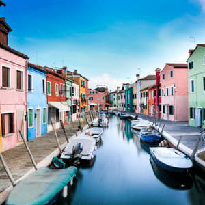 Un canal tranquilo refleja casas de colores vivos y barcos amarrados bajo un cielo azul despejado.
