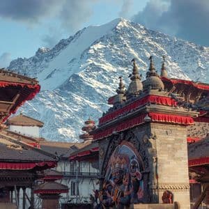 Des temples ornés à plusieurs niveaux se dressent sur une place avec une grande montagne enneigée s'élevant en arrière-plan.