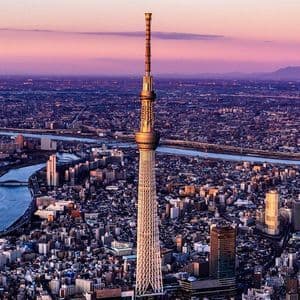 Una torre di trasmissione svetta su un'ampia città attraversata da un fiume sinuoso, vista aerea al tramonto.