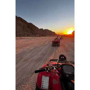 Vista in prima persona da un quad rosso durante un viaggio di gruppo WeRoad su una pista sabbiosa nel deserto al tramonto, con montagne sullo sfondo.