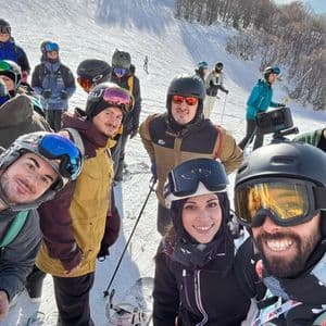 A WeRoad group trip in ski gear smiling for a selfie on a snowy mountain slope.
