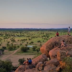 Viaggio di gruppo WeRoad per ammirare il tramonto da grandi massi con vista su una vasta savana punteggiata di alberi.