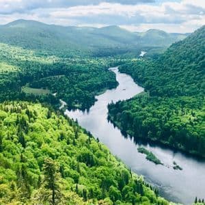 Vue aérienne d'une large rivière serpentant à travers une vaste vallée couverte de forêts verdoyantes et de collines vallonnées.