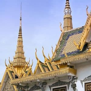 Vue détaillée des flèches dorées ornementées et des toits en tuiles d'un temple de style cambodgien traditionnel, sous un ciel bleu clair.