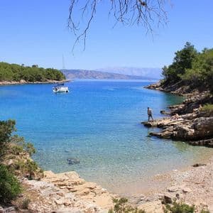 Ein Segelboot ankert in einer abgelegenen Bucht mit klarem türkisfarbenem Wasser, umgeben von felsigen Küsten und Pinienbäumen.