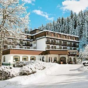 Un edificio alberghiero in stile alpino è circondato da neve alta e da una fitta foresta di pini coperti di neve.