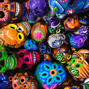 Vue plongeante rapprochée de nombreux crânes Calavera colorés, peints à la main, avec des motifs floraux et géométriques complexes.
