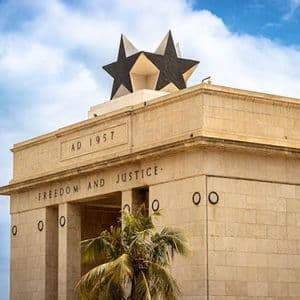 Un grande monumento in pietra sormontato da una stella nera, inciso con 'AD 1957' e 'LIBERTÀ E GIUSTIZIA', sotto un cielo nuvoloso.