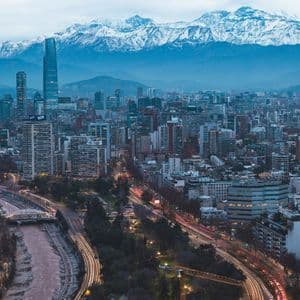 Un denso panorama urbano con edifici illuminati al tramonto, sullo sfondo di grandi montagne innevate.