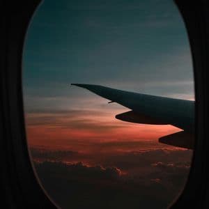 Vue depuis le hublot d'un avion, l'aile survolant les nuages sous un coucher de soleil rouge et orange.