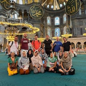 Un gruppo WeRoad posa per una foto su un tappeto verde all'interno di una grande moschea ornata con grandi lampadari.