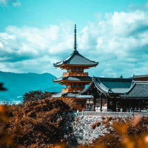 Una tradizionale pagoda a più livelli sorge su una collina che domina una città e le montagne sotto un cielo nuvoloso.