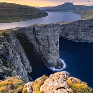 Un grande lago si trova sull'orlo di un'alta scogliera, apparentemente fluttuante sopra le scure acque dell'oceano che si infrangono contro le rocce sottostanti.