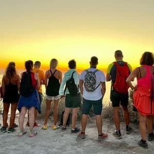 Un gruppo WeRoad con zaini in spalla su una scogliera, ammira il tramonto dorato sul mare.