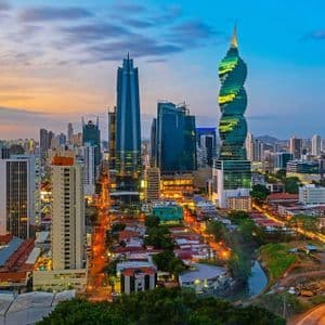 Uno skyline cittadino illuminato con moderni grattacieli, inclusa una distintiva torre ritorta, sotto un vibrante cielo al tramonto.