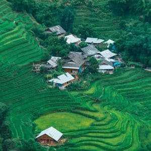 Una vista aérea de un pequeño pueblo enclavado entre vibrantes arrozales aterrazados de color verde que cubren colinas onduladas.