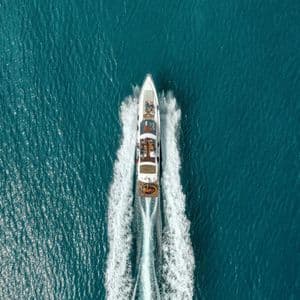Vista aerea di un viaggio di gruppo WeRoad su uno yacht a motore bianco che sfreccia nell'acqua turchese, creando una scia schiumosa.