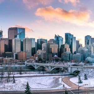Uno skyline cittadino con alti edifici in vetro domina un fiume e un ponte, con terreno coperto di neve in primo piano.