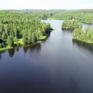 Una vista aerea di un lago blu scuro che si snoda attraverso una vasta e fitta foresta verde, con una piccola barca che naviga in lontananza.